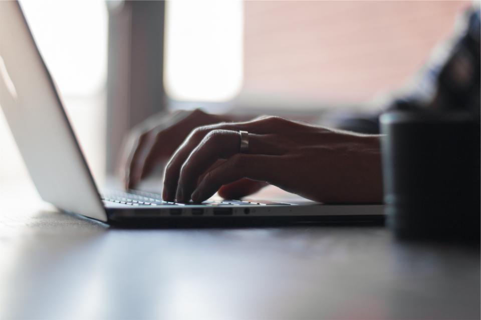 Hand tippt am Laptop an einem Online-Antrag